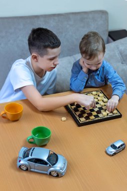 İki Kardeş Evde Dama Oynuyor. İki kardeş ahşap bir masada oturmuş dama oynuyorlar. İki kardeş tahta bir masada oturmuş dama oynuyorlar..