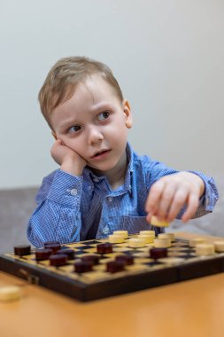 Dama oynarken düşünen genç bir çocuk. Mavi kareli gömlekli genç bir çocuk dama oynuyor, başını elinde dinlendiriyor, düşünceli ve odaklanmış görünüyor..