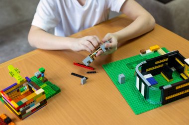 Çocuk renkli plastik tuğlaları birleştiriyor, ahşap bir masa üzerinde yaratıcı yapılar inşa ediyor.