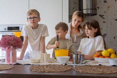 Anne ve çocuklar mutfakta birlikte yemek pişiriyorlar. Bir anne ve üç çocuğu modern bir mutfakta birlikte yemek pişiriyorlar. Aile malzemeleri karıştırıyor, birlikte güzel vakit geçiriyorlar..