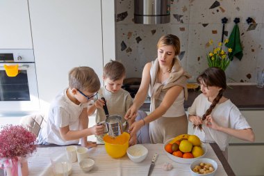 Anne ve çocuklar mutfakta birlikte yemek pişiriyor, ailece güzel vakit geçiriyorlar.