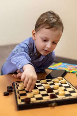 Genç çocuk evde dama oynuyor. Mavi gömlekli genç bir çocuk masada dama oynarken konsantre oluyor. Bir sonraki hamlesini dikkatlice yapıyor.
