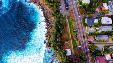 Hawaii 'deki sahil yolunun havadan görüntüsü. Hawaii 'deki bir kıyı yolunun çarpıcı hava manzarası tropik yerleşim yerinin yanındaki kayalık kıyılara çarpan dalgaları gösteriyor.