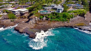 Rocky Hawai sahilindeki lüks okyanus manzaralı evler. Bereketli yeşillik ve turkuaz sularla çevrili kayalık bir Hawaii sahil şeridine tünemiş lüks okyanus manzaralı evler.