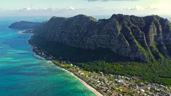 Engebeli Hawaii Kayalıklarının Altındaki Sahil Kasabası. Berrak turkuaz Hawaii kıyı şeridi boyunca sarp yeşil uçurumların dibinde yuva yapmış tropikal bir sahil kasabasının hava manzarası.
