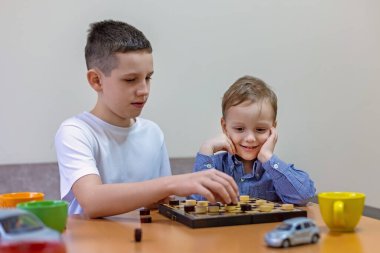 Evde dama oynayan iki kardeş. Büyük ve küçük kardeşler, rahat bir evde oyun oynayarak, masada birlikte dama oynamanın keyfini çıkarırlar..