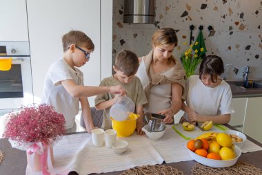Anne ve çocuklar birlikte yemek hazırlıyorlar. Bir anne ve üç çocuğu parlak bir mutfakta birlikte çalışıyorlar. Meyve pişirip kesiyorlar, kaliteli aile zamanlarının tadını çıkarıyorlar.