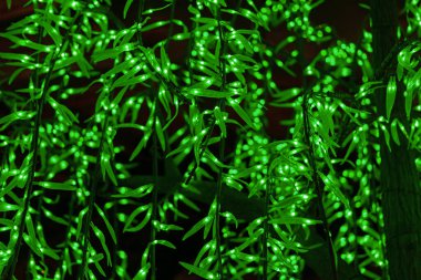 Dallardaki yeşil dekoratif LED ışıklarına yakın çekim. Dalların etrafına sarılmış yapraklara benzeyen sayısız yeşil LED sicim ışıklarının detaylı bir yakın çekimi