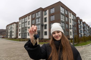 Gülümseyen kadın modern apartman kompleksinin önünde anahtarlarını tutuyor.