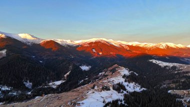Village ile Sunset 'teki Karlı Dağ Manzarası. Gün batımının ılık renkleriyle aydınlanan karla kaplı dağların nefes kesici hava manzarası vadide yuva yapmış küçük bir köy.