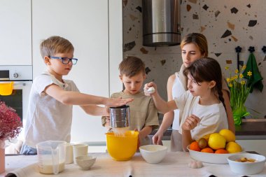 Çocuklar aileleriyle mutfakta yemek pişiriyor. Bir grup çocuk modern mutfakta yetişkin gözetimiyle yemek pişiriyor, malzemeleri karıştırıyor ve evde birlikte yemek yapmayı öğreniyorlar.