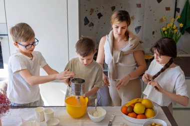 Anne ve çocuklar mutfakta birlikte yemek pişiriyorlar. Bir anne ve çocuklarının malzemelerini hazırladığı, kaliteli zaman geçirdiği ve mutfak becerilerini öğrendiği bir aile pişirme sahnesi.