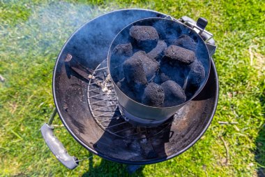 Kömür bacası mangal partisi için ısınıyor. Arka bahçedeki ızgarada sigara içen siyah kömürle dolu baca açıcı yaz barbekü seansına hazırlanıyor.
