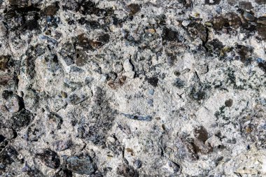 Yıpranmış dokusu olan sert beton bir yüzey. Yıpranmış beton bir yüzeye yakın çekim. Kaba dokuyu, gömülü taşları ve elementlere maruz kalmaktan kaynaklanan doğal çatlakları gösteriyor.