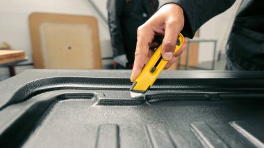 Dokulu yüzeyde kullanılacak alet bıçağıyla yakın plan çekimde. Yakından çekilmiş bir resim sarı bir bıçak tutan bir insanın elini gösteriyor, desenli siyah bir yüzeyi dikkatlice kesiyor.