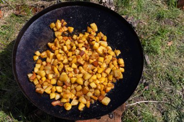 Skillet 'te Kızarmış Patates Pişirme. Açık havada siyah bir tavada kızartılmış altın kahverengimsi patateslerin yakın çekimi, kırsal açık hava yemekleri ve lezzetli ev yapımı yemekler sergileniyor.