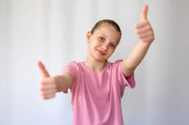Gülümseyen kız çifte onay veriyor. Pembe gömlekli, kendine güvenen, gülümseyen ve her iki başparmağını da gösteren genç kız, beyaz arka planda onay ve pozitifliği ifade ediyor.