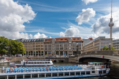 Berlin, 26.05.2025, Nehir tekneleri ve Berlin TV Kulesi, Güneşli Gün. Turist tekneleri, Berlin TV Kulesi ve arka planda canlı bir gökyüzünün altında tarihi binalarla birlikte Spree Nehri 'nde geziniyor.