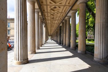 Berlin, 26.05.2025, Derin Perspektifli Sunlit Klasik Kolonnade. Flütlü sütunları ve geometrik tavanı olan parlak taş sütunlar, uzun gölgeler bırakıyor ve uzaktaki bir kaybolma noktasına doğru yol alıyor..