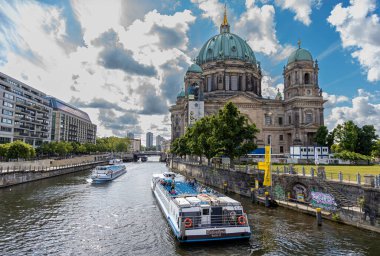 Berlin, 26.05.2025, Berlin Katedrali 'nden geçen tur botları. Berlin Katedrali 'nin önünden geçen nehir tekneleri dramatik bulutlu gökyüzünün altında, tarihi ve modern Berlins harmanı sergiliyor.