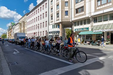 Almanya, Berlin, 26.05.2025, grup bisiklet turu şehir trafiği caddesinde. Rehberli bir grup bisikletçi, güneşli bir gökyüzü altında trafik ve kentsel binalarda gezinerek Almanya 'nın bir şehir caddesi boyunca ilerliyorlar.