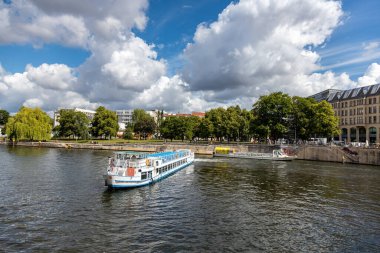 Almanya, Berlin, 26.05.2025, Berlin Spree 'de nehir teknesi. Berlin 'deki Spree Nehri boyunca gezen tekneler parçalı bulutlu bir günde ağaçların, tarihi binaların ve şehir hayatının yanından geçiyor.