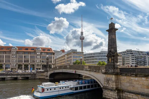Almanya, Berlin, 26.05.2025, Berlin TV kulesi ve köprüsü olan şehir manzarası. Berlin 'deki Spree Nehri' nde tarihi bir köprünün altından bir tur teknesi geçiyor. Arkasında ikonik televizyon kulesi ve modern binalar var..