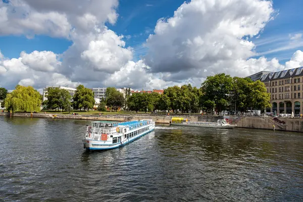 Almanya, Berlin, 26.05.2025, Berlin Spree 'de nehir teknesi. Berlin 'deki Spree Nehri boyunca gezen tekneler parçalı bulutlu bir günde ağaçların, tarihi binaların ve şehir hayatının yanından geçiyor.