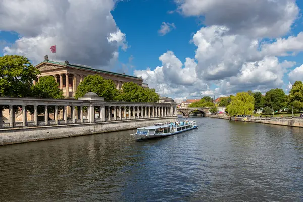 Almanya, Berlin, 26.05.2025, Berlin müzesinin yanından geçen turist gemisi. Modern bir gezi teknesi Spree Nehri boyunca yelken açar, Müze Adası 'nın simgelerinden geçer ve dramatik bulutların altında yemyeşil bir yer bulur..