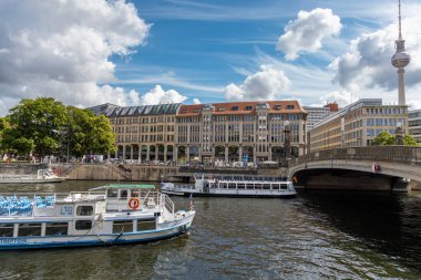 Almanya, Berlin, 26.05.2025, Berlin 'deki Spree Nehri' nde gezi gemileri. Spree Nehri boyunca bir köprü ve modern binaların yakınında turist tekneleri dolaşırken, Berlin TV Kulesi arka planda görülüyor.