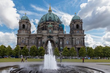 Almanya, Berlin, 26.05.2025, Çeşme ve Turistlerle Berlin Katedrali. Berlin Katedrali manzarası, etkileyici kubbeleri, merkezi bir çeşmesi ve ön planda yürüyen ziyaretçileri olan Berliner Dom..