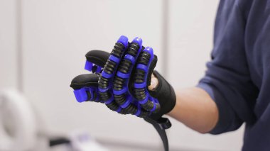 Mavi ve siyah robotik rehabilitasyon eldiveninin yakın çekimi. Bir insan el rehabilitasyonu için tasarlanmış yüksek teknolojili bir robot eldiven giyer, hareket ve motor işlevlere yardımcı olması için parmakları boyunca esnek mavi ve siyah aktivatörler bulunur..