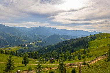 Kırsal köy manzaralı dağ vadisi manzarası. Yeşil tepeleri, orman yamaçları ve dramatik, parçalı bulutlu gökyüzünün altında küçük bir köy olan manzaralı dağ vadisi.