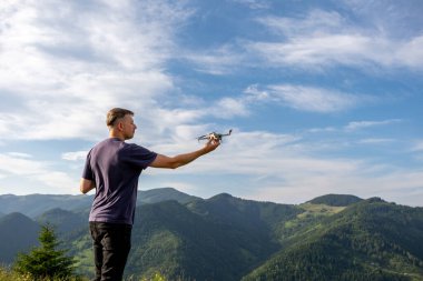 Dağ manzarasına insansız hava aracı fırlatan adam. Bir adam yeşil tepeler ve mavi gökyüzüyle çevrili manzaralı bir dağ sırtında dururken insansız hava aracı fırlatmaya hazırlanıyor.