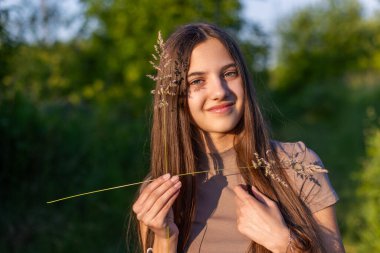 Yüzünde çimen gölgesi olan güzel bir kız. Güneşin altında duran güzel bir kız, vahşi otlarla yüzünde narin bir gölge oluşturarak doğal bir sanatsal etki yaratıyor.