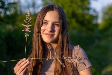 Gün ışığında yüzünde çimen gölgesi olan kız. Genç bir kız hafifçe gülümsüyor. Vahşi otların narin gölgesi gibi. Sıcak altın saat güneşi yüzüne vuruyor.