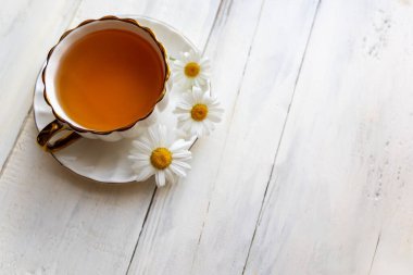 Papatya çayı ve papatya çayı. Papatya çayıyla dolu porselen bir fincanın üst görüntüsü, kırsal beyaz ahşap bir masada taze papatyalarla çevrili.