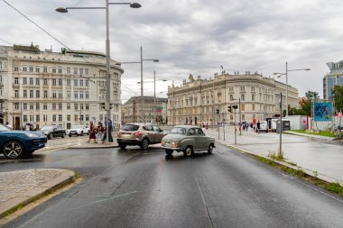 Viyana, Avusturya - 01 Ağustos, 2025. Viyana 'da yağmurlu bir günde tarihi binalar ve trafik. Viyana 'nın merkezinde klasik ve modern arabaların, yayaların ve bulutlu, ıslak gökyüzünün altındaki büyük tarihi binaların olduğu bir sokak sahnesi..