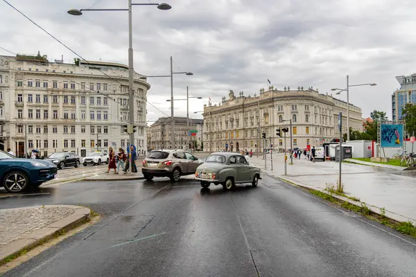 Viyana, Avusturya - 01 Ağustos, 2025. Viyana 'da yağmurlu bir günde tarihi binalar ve trafik. Viyana 'nın merkezinde klasik ve modern arabaların, yayaların ve bulutlu, ıslak gökyüzünün altındaki büyük tarihi binaların olduğu bir sokak sahnesi..