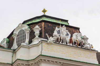 Avusturya Ulusal Kütüphanesi, Viyana, Avusturya - 01 Ağustos, 2025. Avusturya Ulusal Kütüphanesi 'ndeki Barok çatı heykeli. Viyana 'daki Avusturya Ulusal Kütüphanesi' ndeki at ve figürlerin dramatik çatı heykeli, klasik Latin yazıtları ve