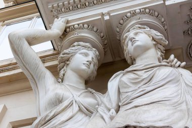 Viyana, Avusturya - 01 Ağustos, 2025. Tarihi bina üzerindeki klasik kadın heykellerinin yakın çekimi. İki zarif beyaz mermer kadın heykeli, klasik Avrupa mimari cephesinde süslü bir çıkıntıyı destekliyor..