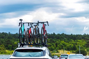 Trafikte çatıda bisikleti olan bir araba. Trafiğin ortasında hareket eden bir arabanın çatı rafına monte edilmiş birkaç bisiklet, bir ormanın arka planına ve bulutlu bir gökyüzüne karşı.
