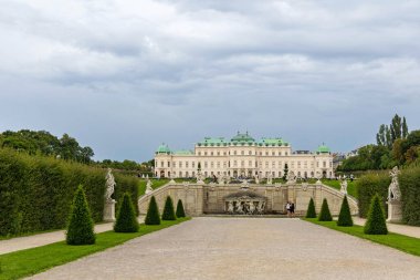 Belvedere Sarayı, Viyana, Avusturya - 01 Ağustos, 2025. Yeşil kubbeleri olan büyük barok tarzı bir saray. Simetrik bir bahçe, heykeller ve bulutlu bir gökyüzünün altında dekoratif bir çeşme tarafından çerçevelenmiş..