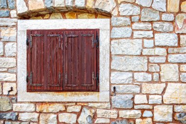Rustic wooden shutter on old stone wall. Close-up of a closed wooden window shutter mounted on a vintage stone wall, showcasing rustic architecture and aged textures