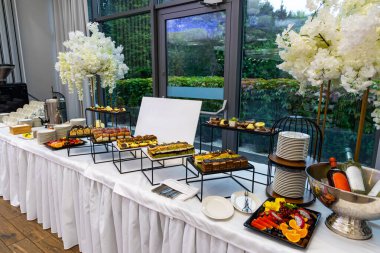 Şarap ve meyveli lüks tatlı büfesi masası. Resmi bir etkinlikte çeşitli tatlılar, taze meyve tabakları, istiflenmiş tabaklar ve soğutulmuş şarap şişelerinin yer aldığı zarif bir büfe düzenleme..