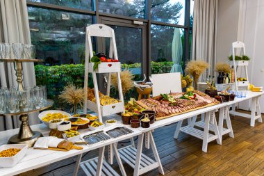 Rustic buffet table with cold cuts, cheese, and appetizers. Elegant buffet setup featuring sliced meats, smoked cheese, breads, olives, pickled vegetables, sauces, and wine in a rustic event setting