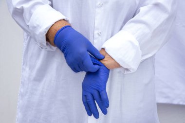 Lateks eldivenli bir doktorun elleri. Doktor bir tıp önlüğünün arka planına karşı steril eldiven giyer. Enfeksiyon kontrol kavramı.