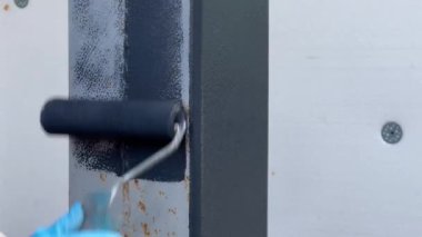 Paslanma önleyici gri boyayla paslanma sütununu boyuyorum. Boya silindirli bir el. Dış onarım. Demir için özel korozyon önleyici boya. Paslı metal yüzey ile gri boya tedavisi. Kavram
