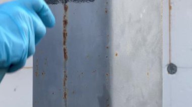 Açık havada çalışan bir sanatçı tarafından paten fırçasıyla metal bir sütun grisi boya. Boya silindirli eldivenli bir el. Dış onarım. Demir için özel korozyon önleyici boya. Paslı tedavinin