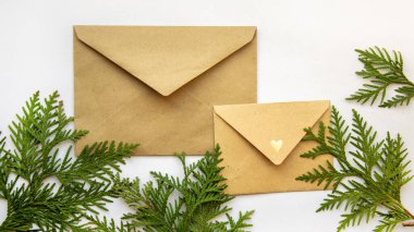 Beyaz bir zemin üzerinde el işi zarfları ve selvi filizleri. Noel arifesi. Yeni yıl tatiline hazırlanıyorum. Noel, bayram ayrıntıları, dekorasyon, hediyeler, ambalaj, yeni yıl atmosferi.